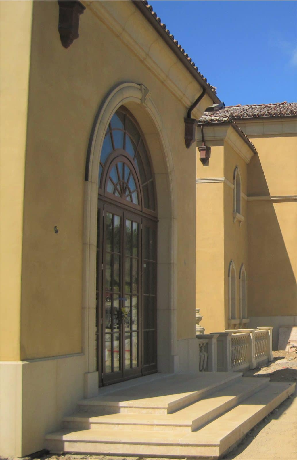 Porte d’entrée cintrée en bois et verre sur une villa méditerranéenne enduite