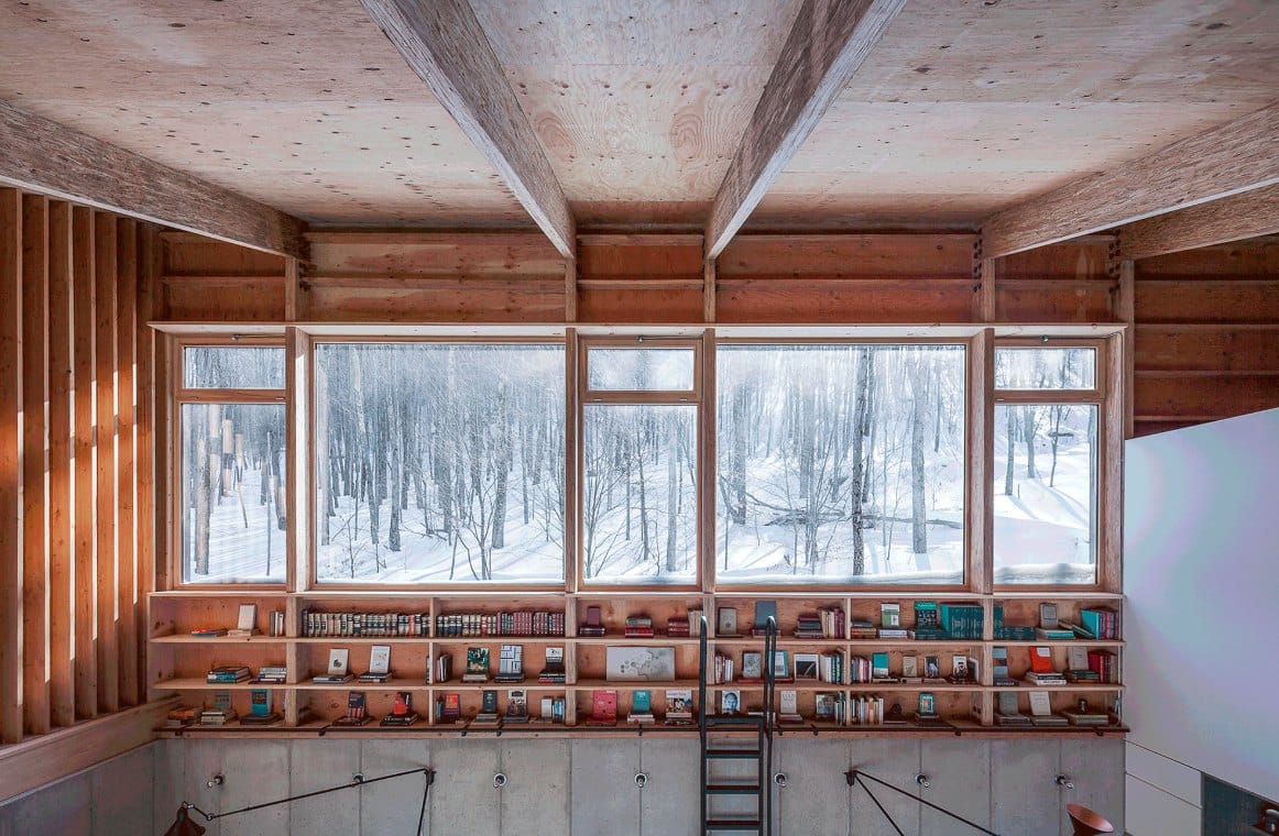 Mur de fenêtres en bois au-dessus des bibliothèques d’une bibliothèque contemporaine, forêt enneigée dehors