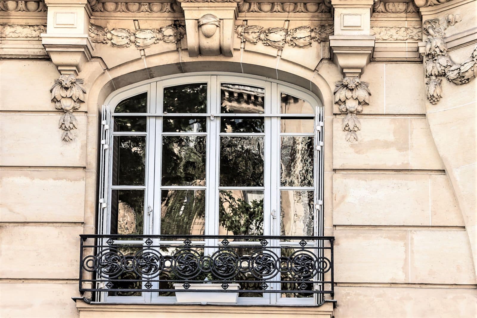 Fenêtre en bois en arc surbaissé sur une façade parisienne en pierre sculptée
