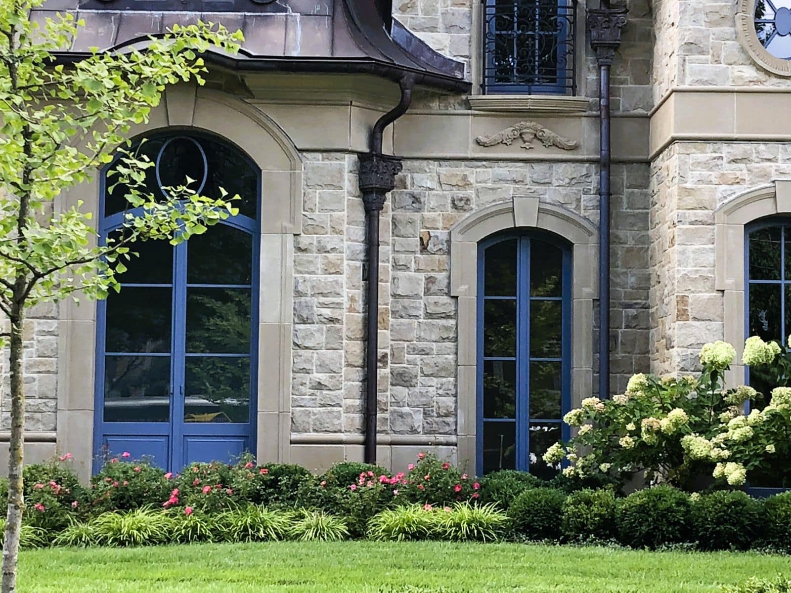 Portes-fenêtres cintrées avec capotage aluminium bleu et œil-de-bœuf rond dans une façade en pierre
