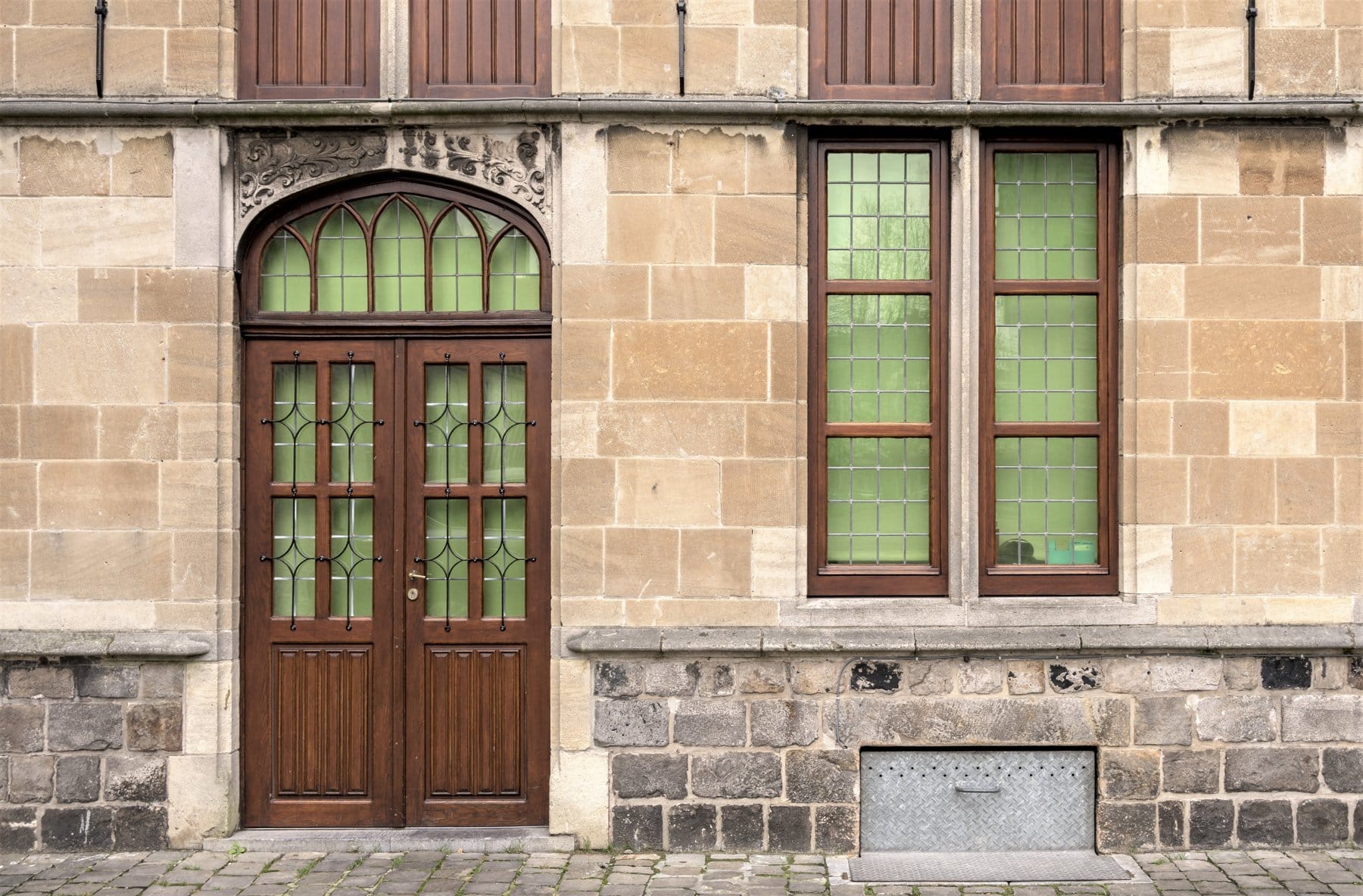 Façade ancienne en pierre avec porte d’entrée double cintrée en bois et hautes fenêtres en bois à vitrail