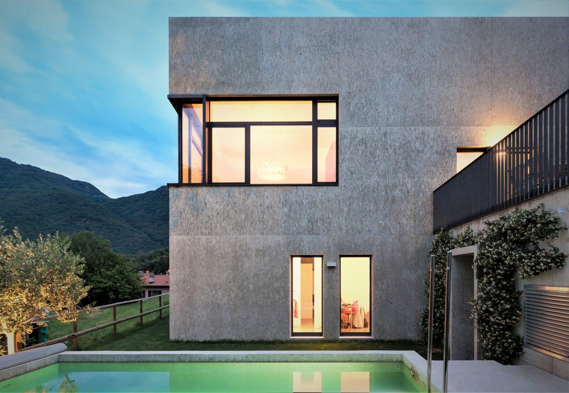 Maison contemporaine d’aspect béton avec fenêtres et porte d’entrée en bois au crépuscule