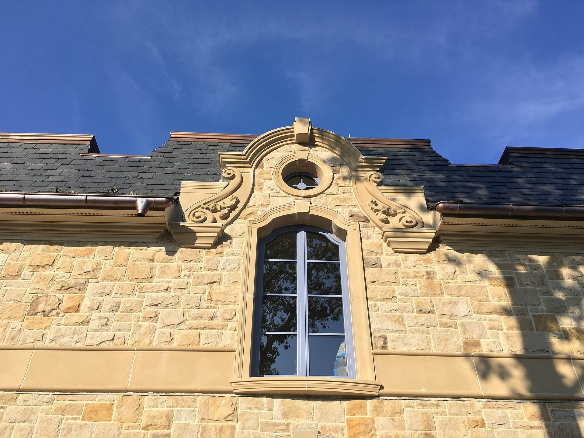 French casement dormer window under a carved limestone pediment on a slate roof, French chateau style home
