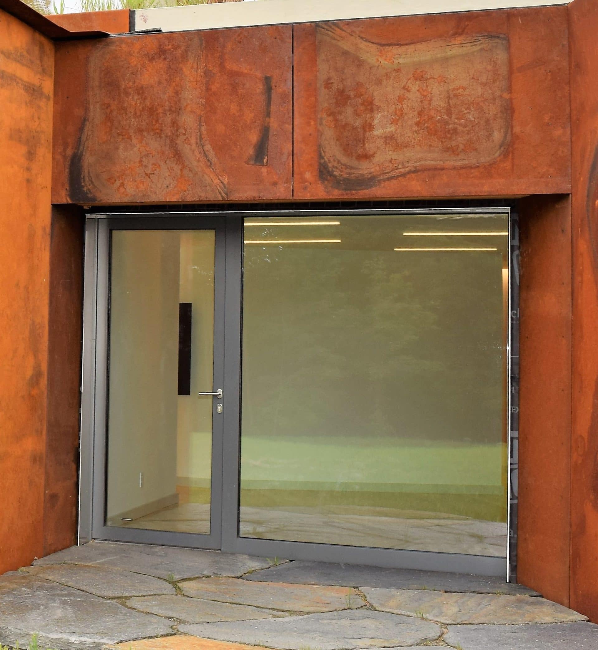 Entrée contemporaine avec porte vitrée dans un encadrement en acier corten